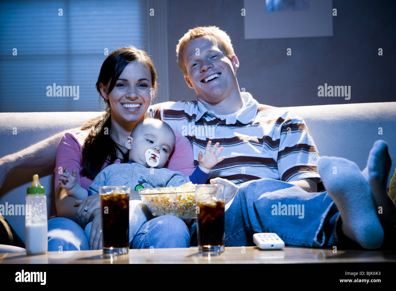 L'homme sur canapé avec femme nourrir bébé et bol de maïs soufflé smiling Banque D'Images