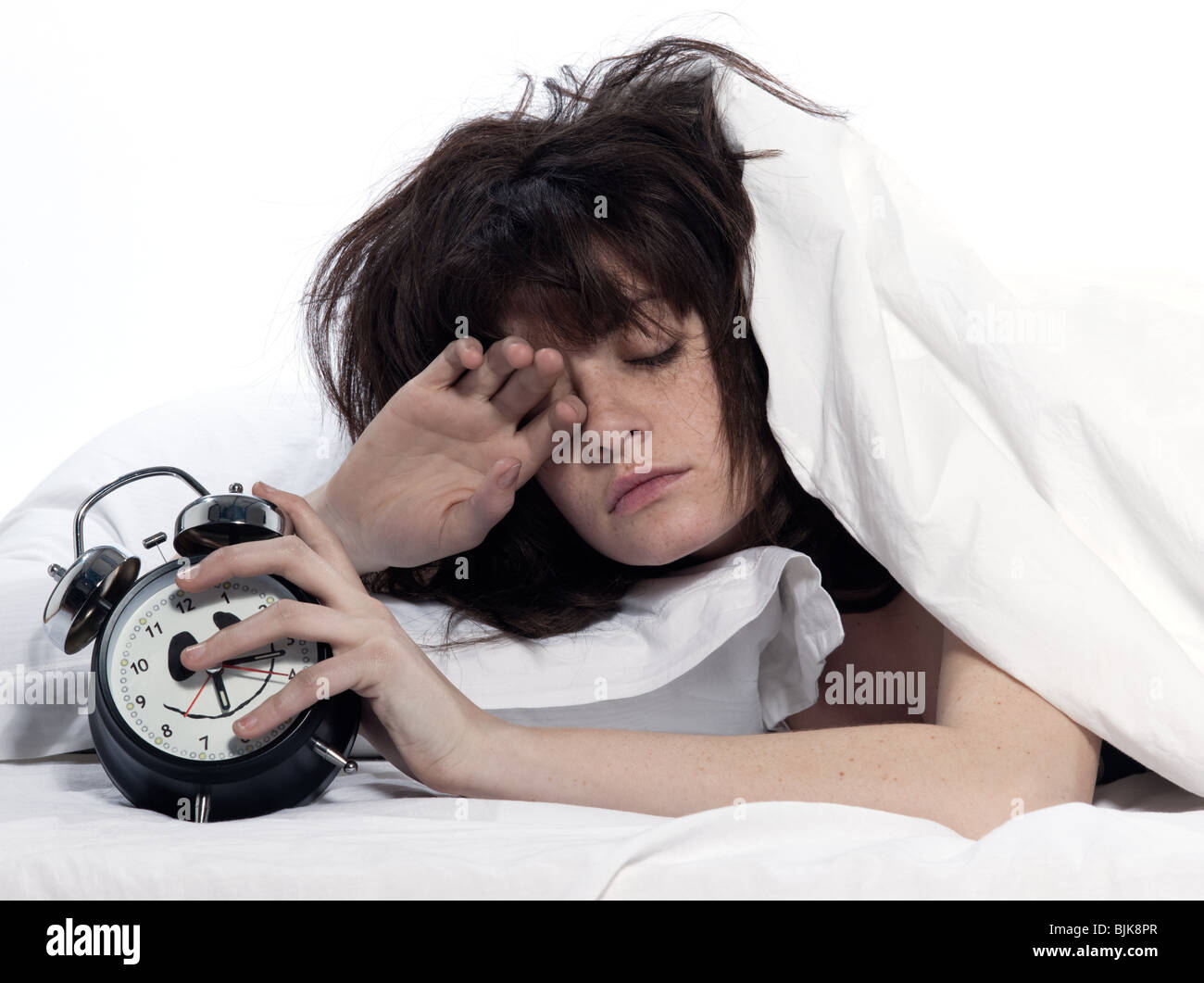 Jeune femme femme au lit l'éveil fatigué maintenant réveil sur fond blanc Banque D'Images