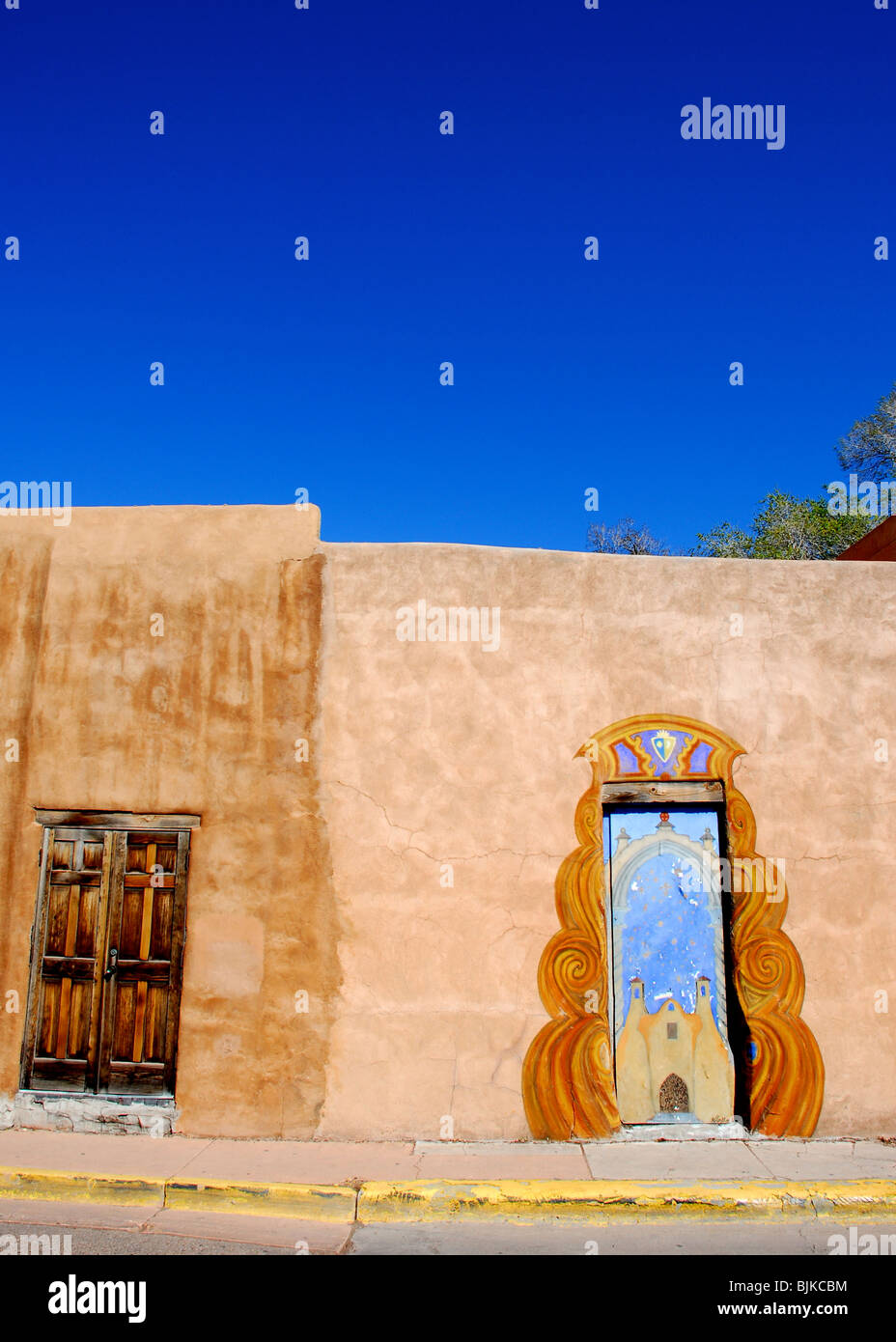 Santa Fe, Nouveau Mexique, USA - Le 20 avril 2008 : porte peint artistiquement et adobe mur avec ciel bleu brillant sur l'après-midi ensoleillé dans le centre-ville de Santa Fe. Banque D'Images