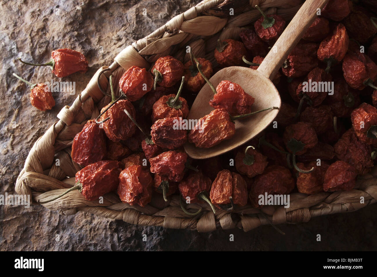 Mini-Peppers (Capsicum) avec une cuillère en bois dans un panier en osier sur une surface en pierre Banque D'Images