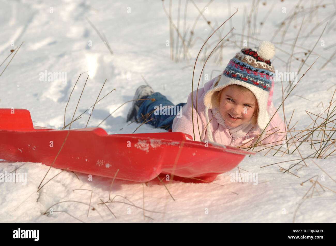 Une jeune fille de maternelle dans un manteau rose bonnet de laine et  s'amusant de la luge dans la neige sur un toboggan rouge Photo Stock - Alamy