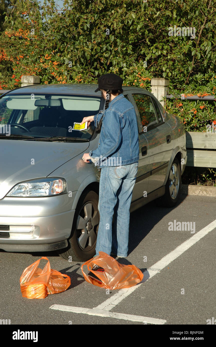 Jeune femme recherche d'une amende de stationnement sur le pare-brise de sa voiture, England, UK Banque D'Images