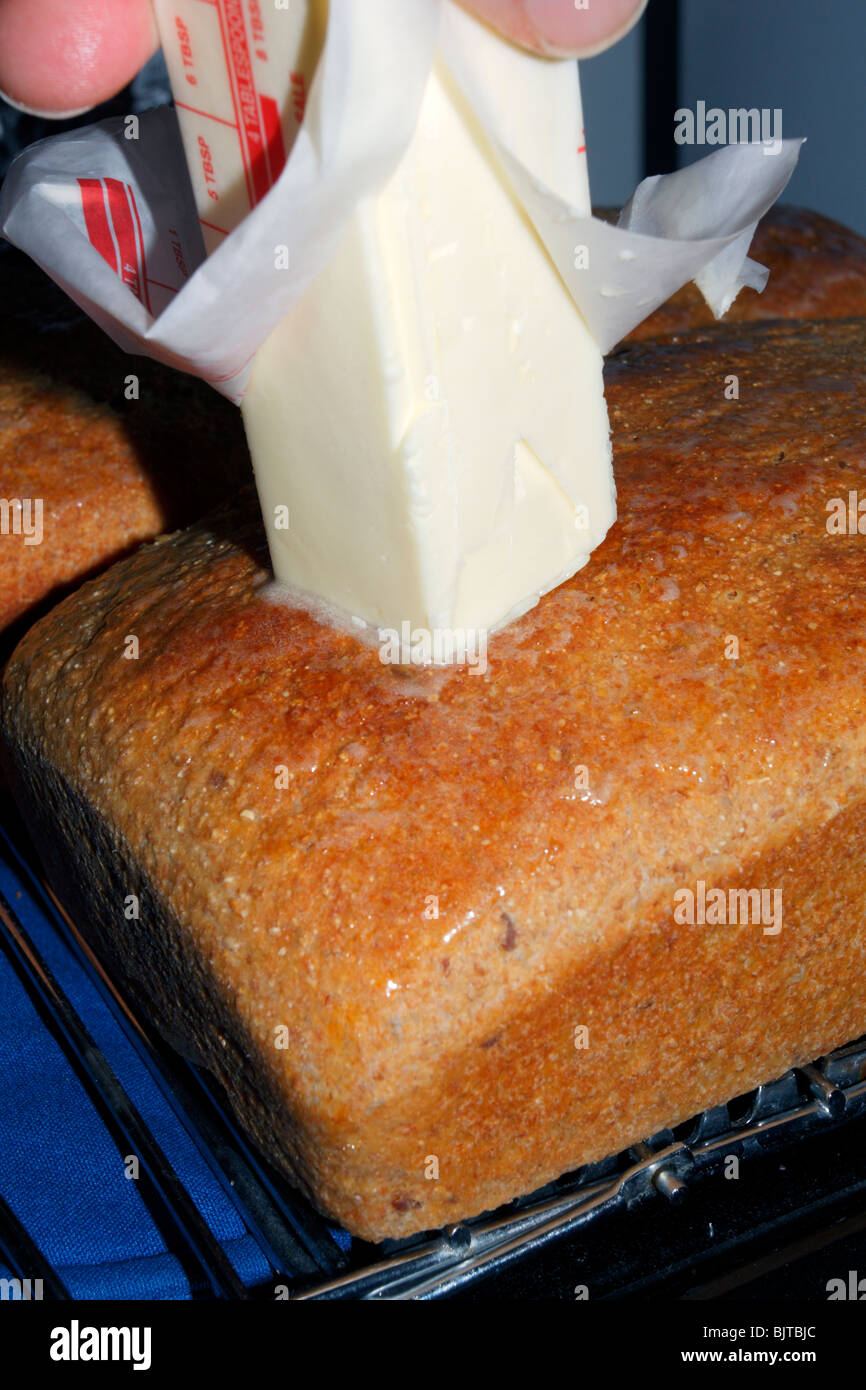 Stick de beurre fondu étant comme assaisonnement et d'étanchéité sur le grenu haut de miche de pain de blé. Banque D'Images