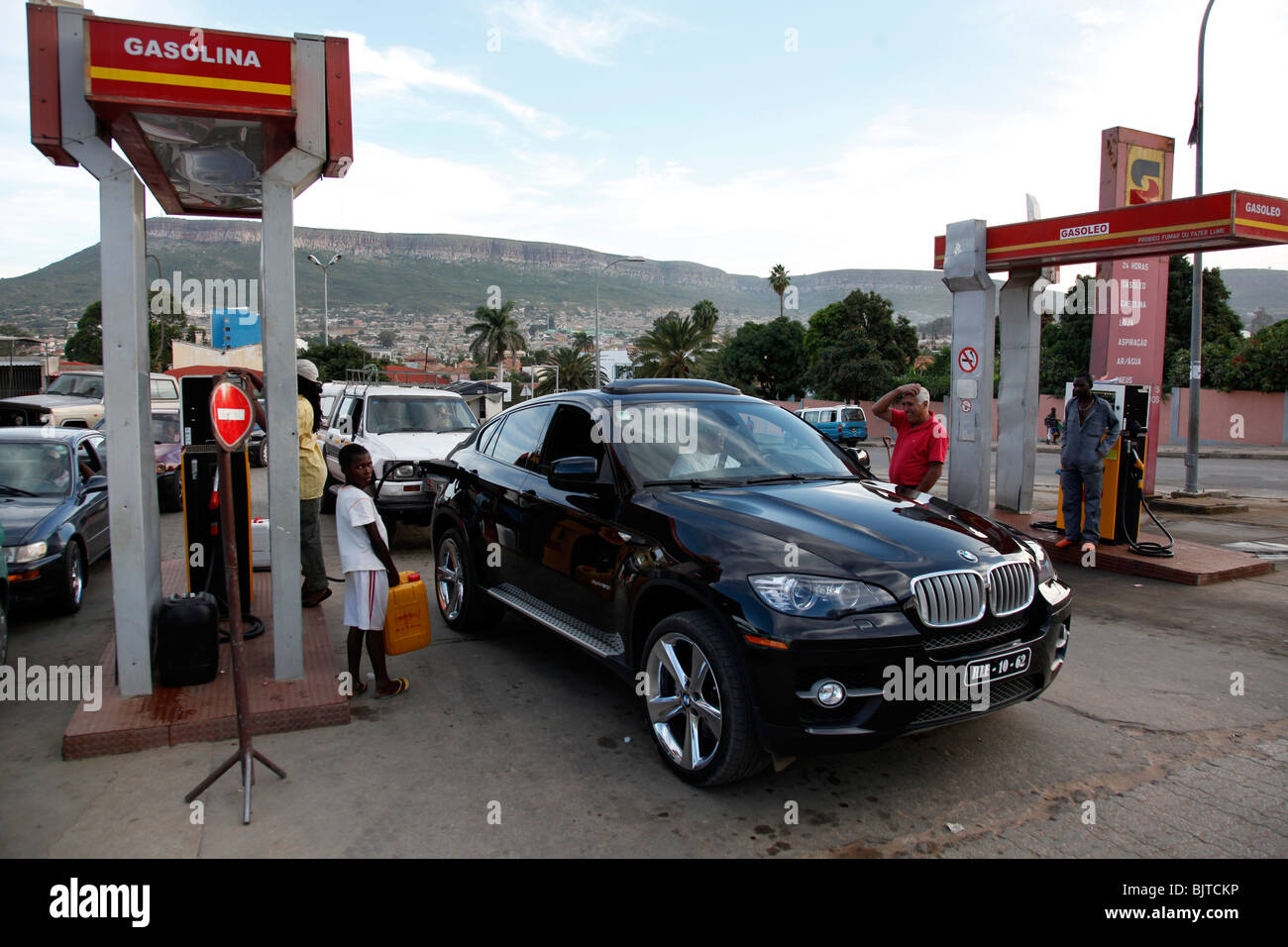 Profitez de l'élite angolaise l'importation de voitures coûteuses alors que les pauvres s'attendent à remplir leur récipient de carburant. Banque D'Images