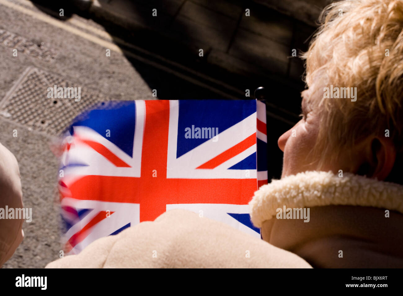 A woman's Union Jack drapeau flotte dans le vent alors qu'elle attend avec impatience l'apparition de la Reine. Banque D'Images