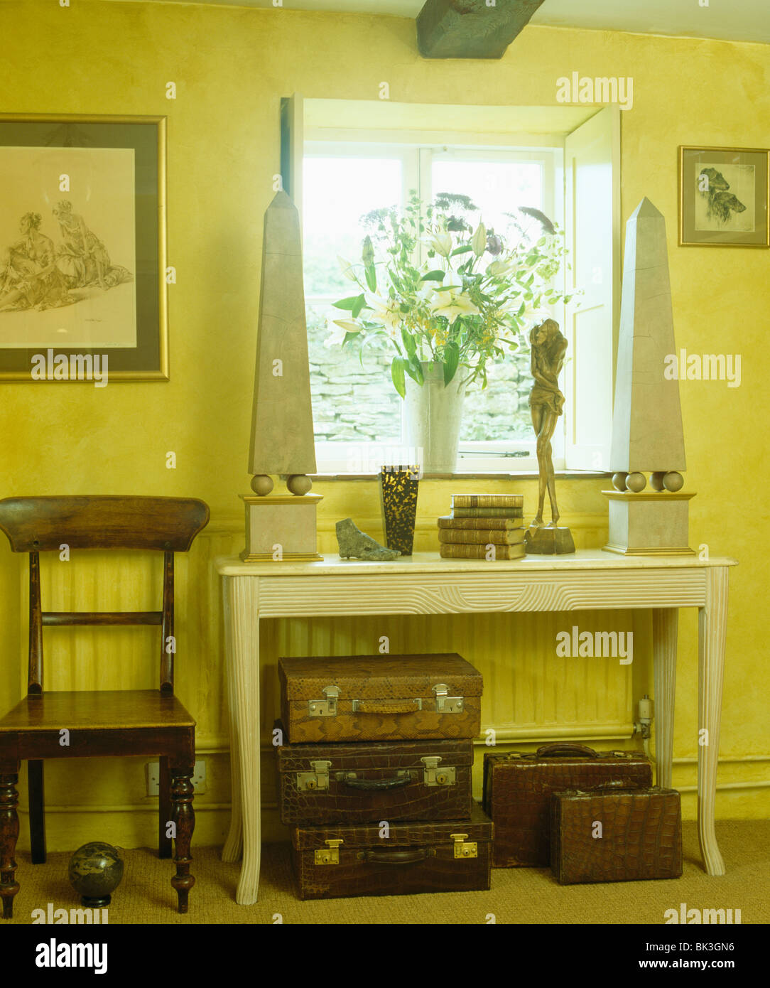 Obélisques de pierre sur table console en jaune pâle avec un hall pays chaise en bois et de vieux cuir valises Banque D'Images