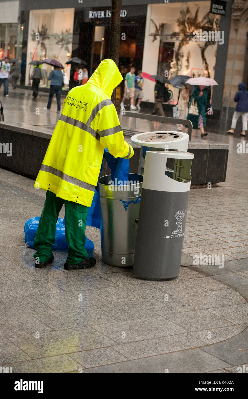 Travailleur du conseil public vider poubelle dans la pluie torrentielle Banque D'Images