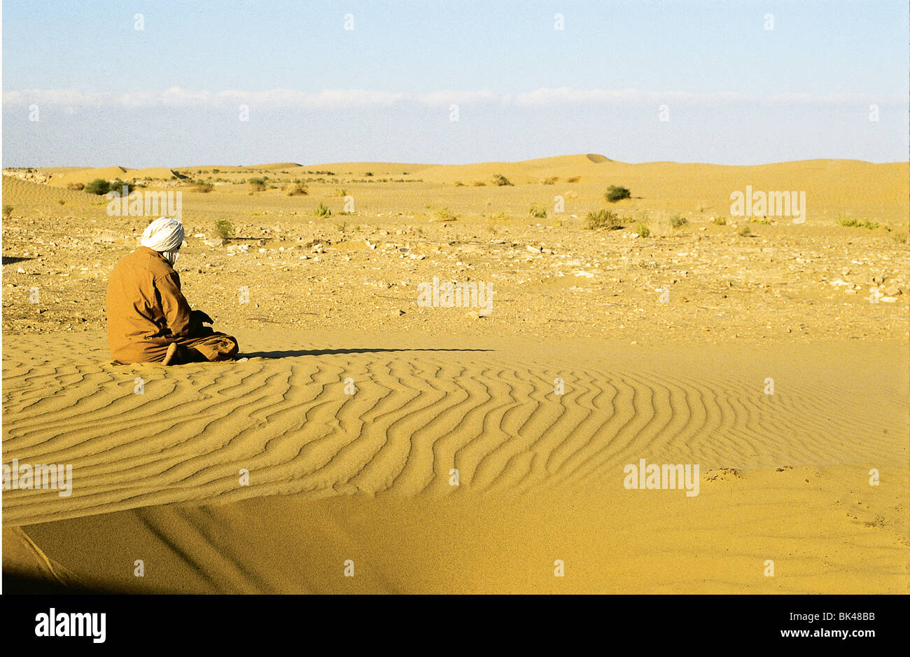 Un homme à genoux à l'opposé du soleil dans le désert du Sahara, Larache, Maroc Banque D'Images