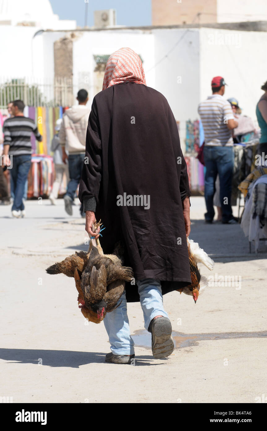 L'homme arabe à marcher le long de la rue avec des poulets morts Banque D'Images