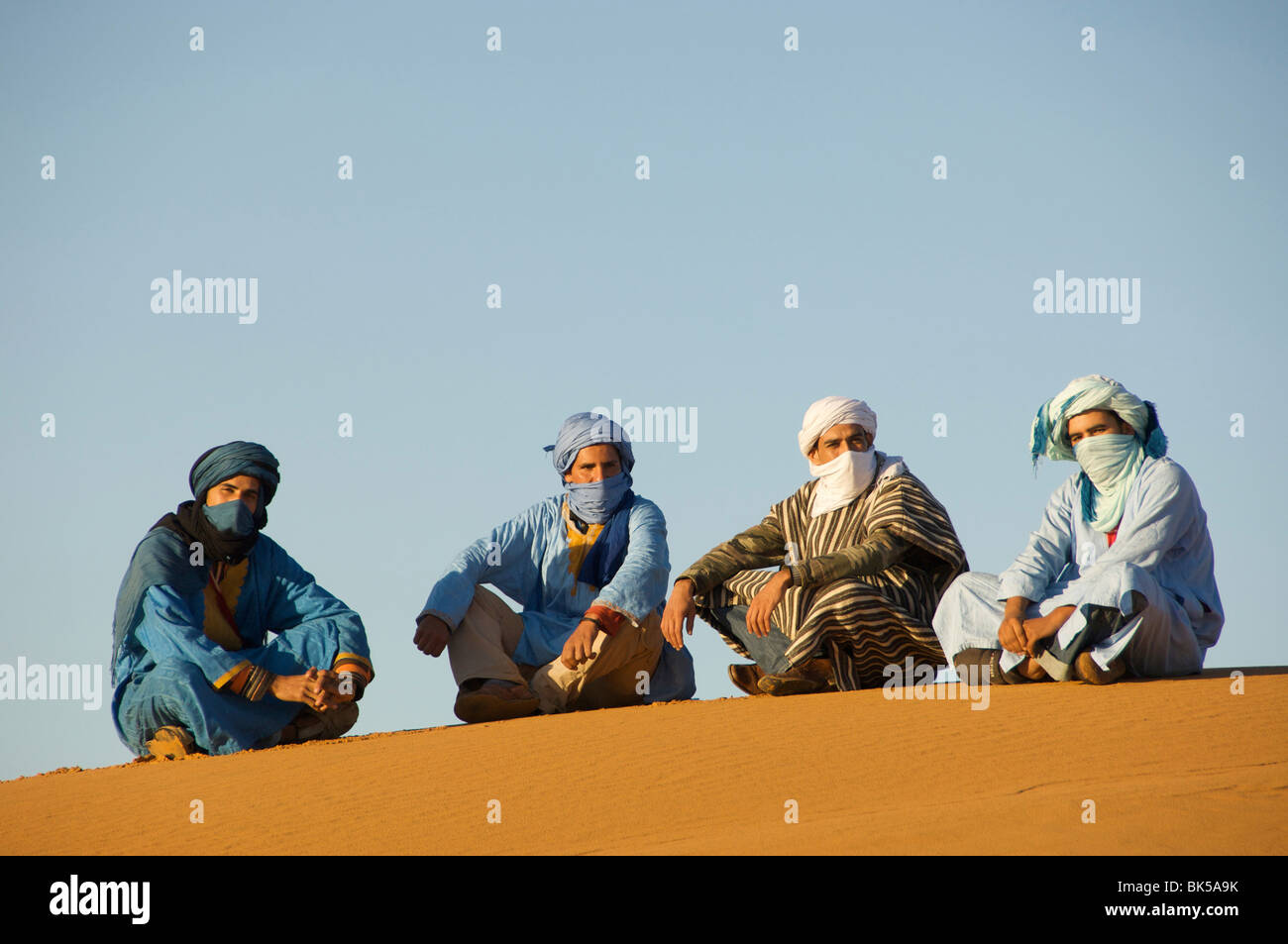 Portrait de quatre hommes touareg assis sur le sable dans un désert, désert du Sahara, Merzouga, Maroc Banque D'Images