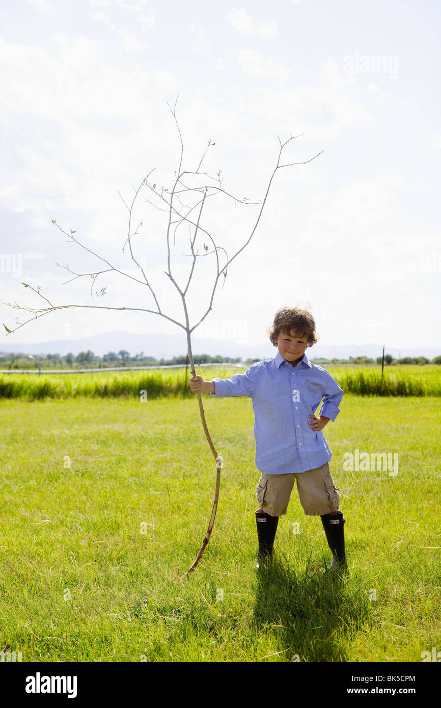 Young boy holding grand bâton dans le champ Banque D'Images