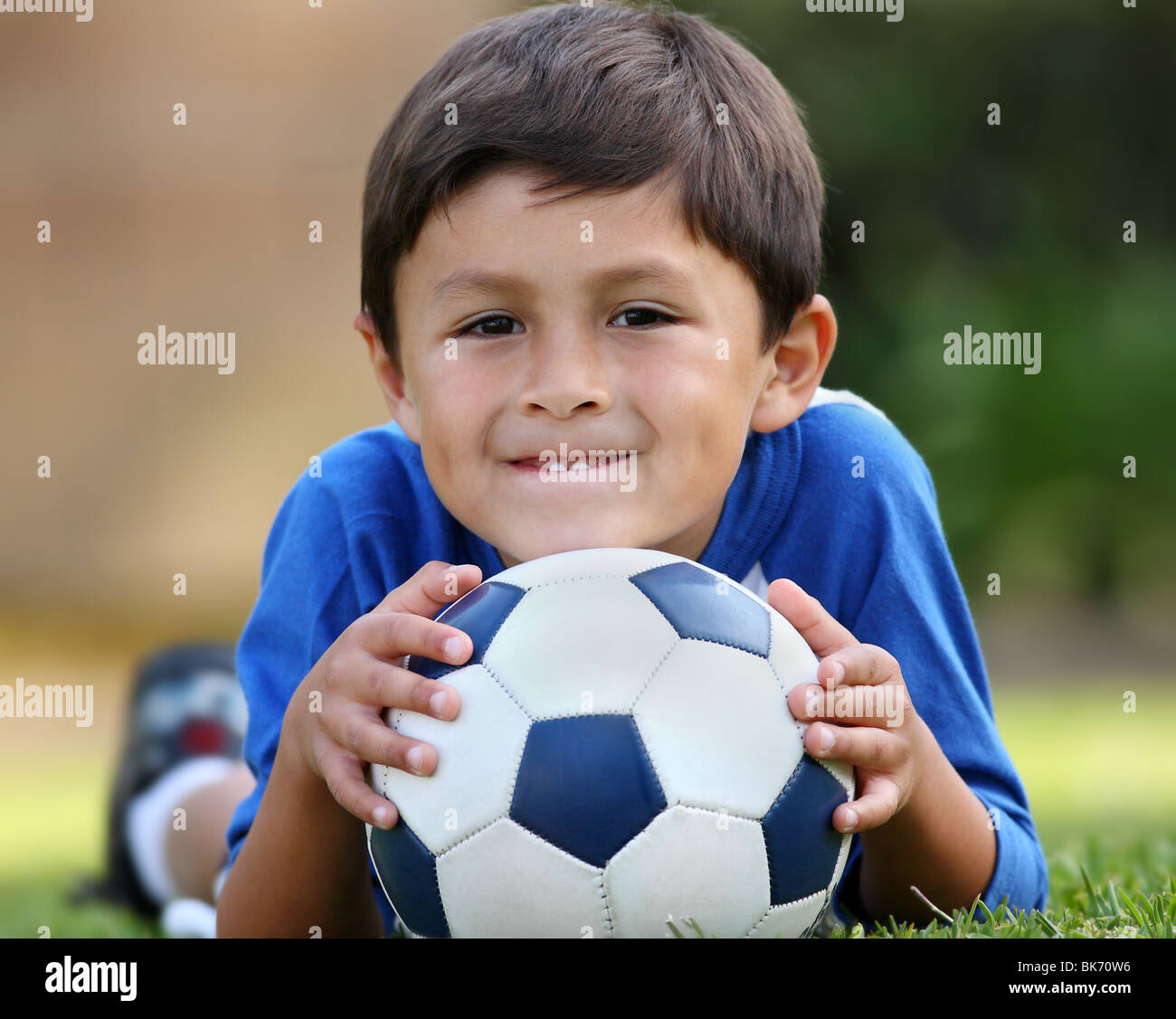 Young brown haired woman in blue shirt allongé sur l'herbe avec ballon de soccer dans les mains Banque D'Images