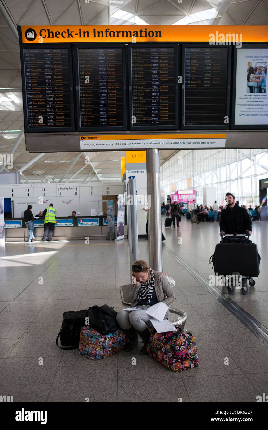 Un passager est assis en dessous d'un enregistrement à l'aéroport d'information montrant tous les vols annulés parlant dans son téléphone portable Banque D'Images