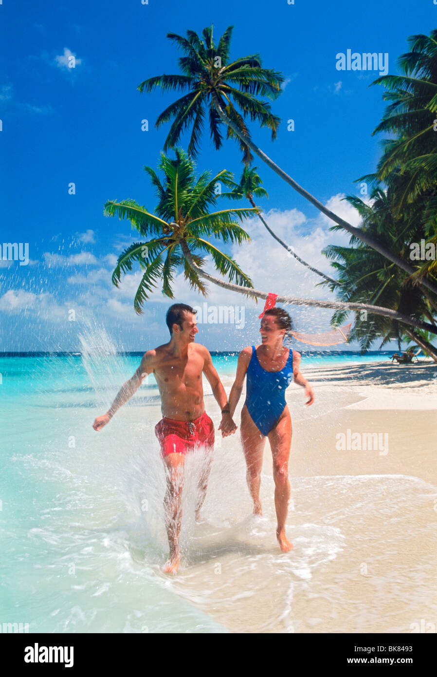 Couple running through le long de vagues de sable sur l'île tropicale Banque D'Images