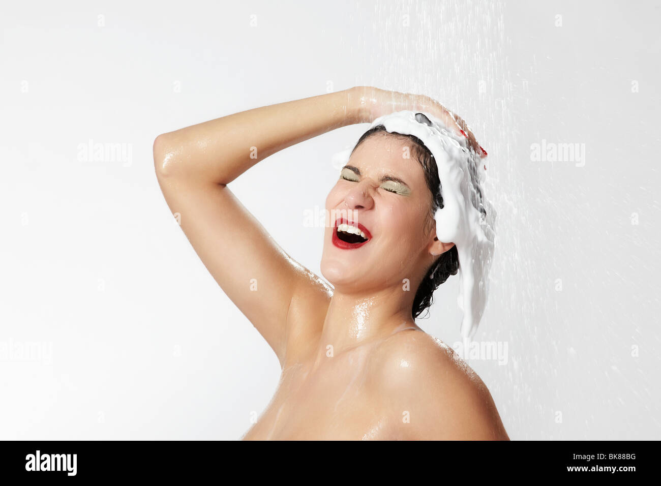 Jeune femme gaie dans la douche avec de la mousse dans les cheveux Banque D'Images