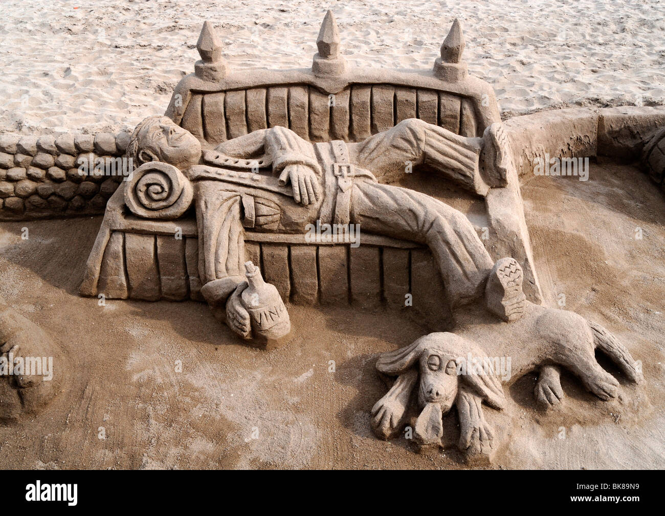 Sculpture de sable d'un clochard avec un chien couché sur un banc Banque D'Images