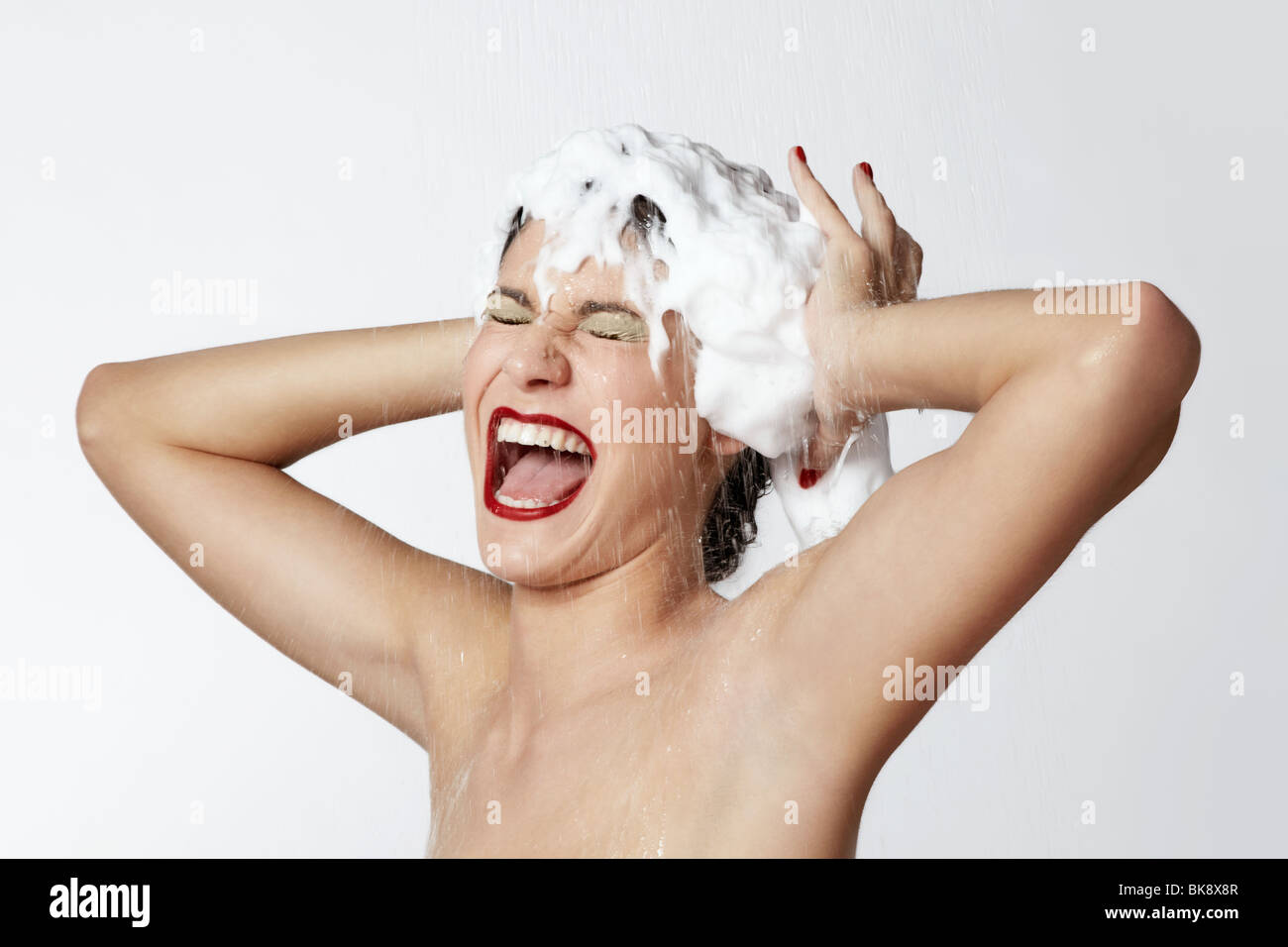 Jeune femme gaie dans la douche avec de la mousse dans les cheveux Banque D'Images