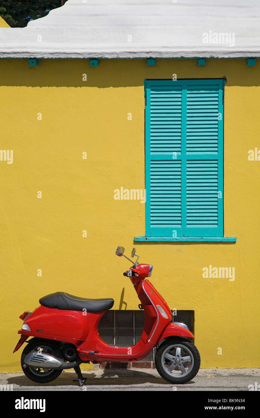 Scooter rouge contre un bâtiment jaune vif à St George's, les Bermudes. Banque D'Images