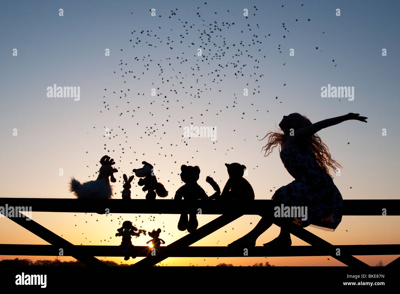 Fille projetant des étoiles sur une poupée de chiffon, le poulet, le renard, le lapin, le chat et les ours en peluche peluches assis sur une barrière au coucher du soleil. Silhouette Banque D'Images