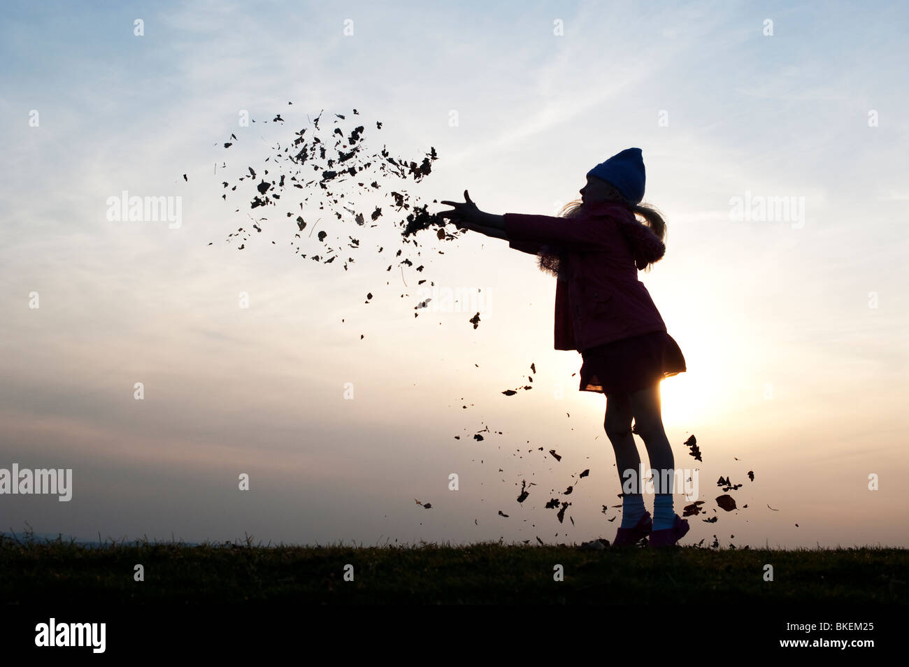 Jeune fille s'amusant de jeter les feuilles. Silhouette Banque D'Images