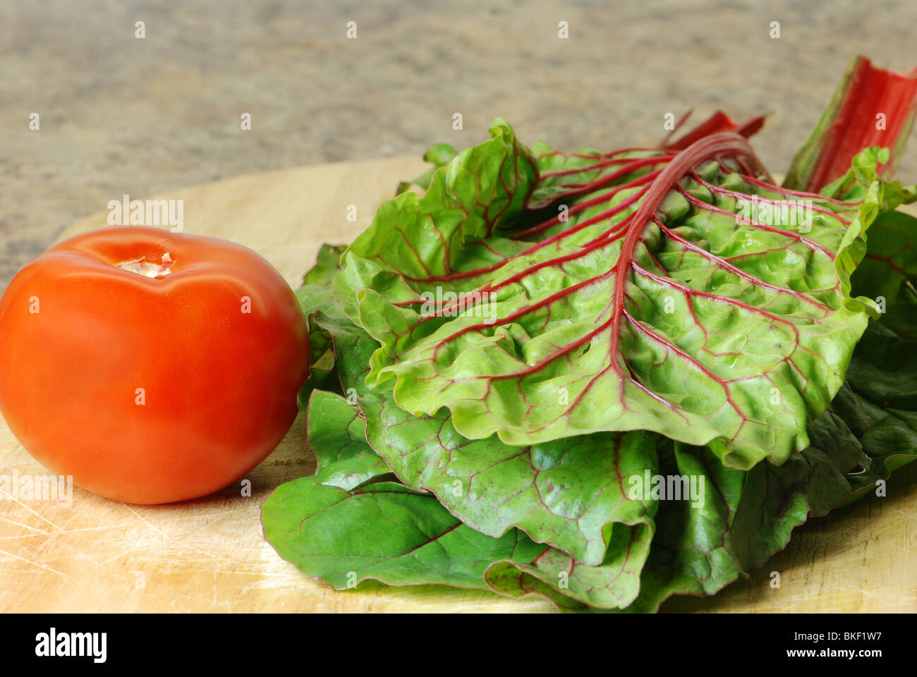 Feuilles de bette à carde rouge et les tomates sur une planche à découper Banque D'Images