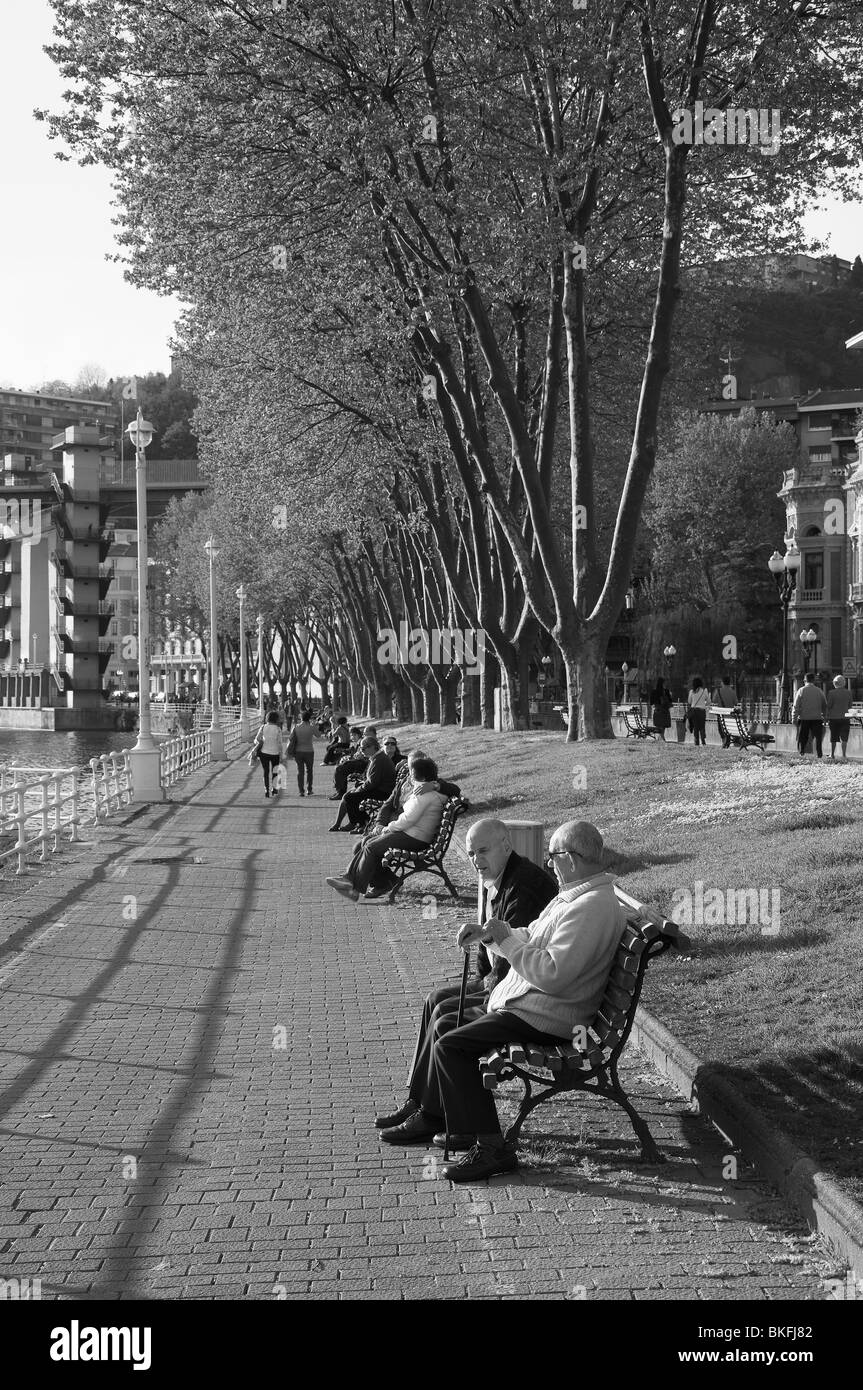 Les personnes âgées assis au soleil sur les rives de la rivière Nervion park dans la ville de Bilbao, Pays Basque, Espagne Banque D'Images