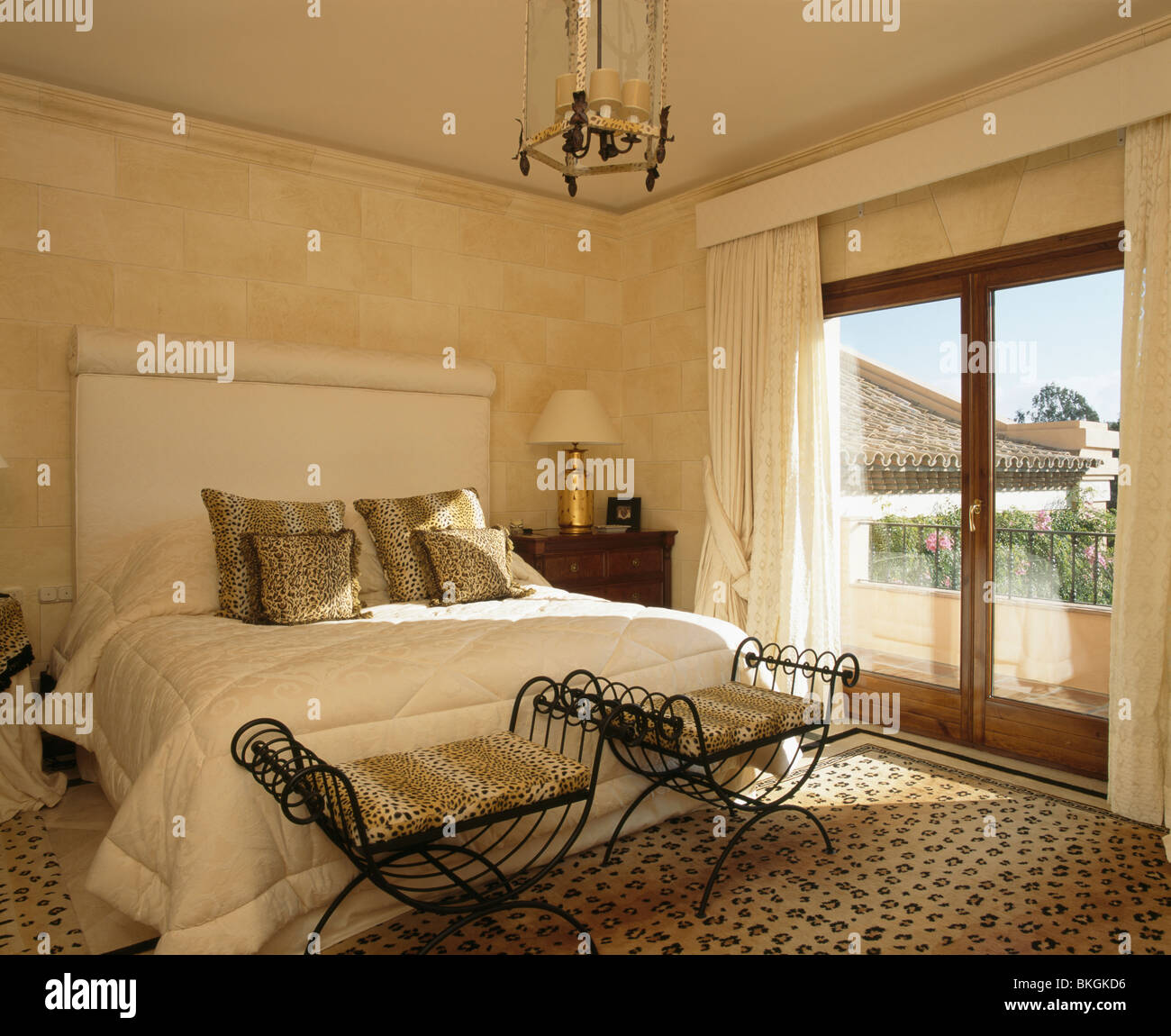 Tabourets en fer forgé au-dessous de lit avec des coussins d'impression  dans la chambre à coucher moderne avec des tapis d'impression et des portes  de balcon Photo Stock - Alamy