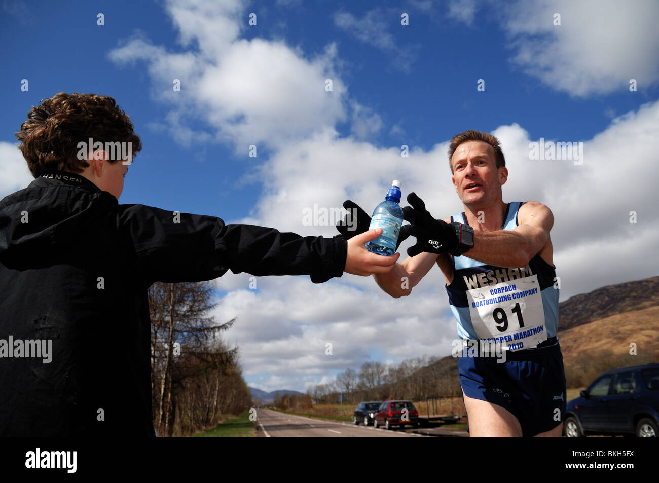 Marathon de Lochaber organisée chaque année par le loch linnie.Runner atteint pour un peu d'eau au cours de la race,de jeune garçon.Sunshine Banque D'Images