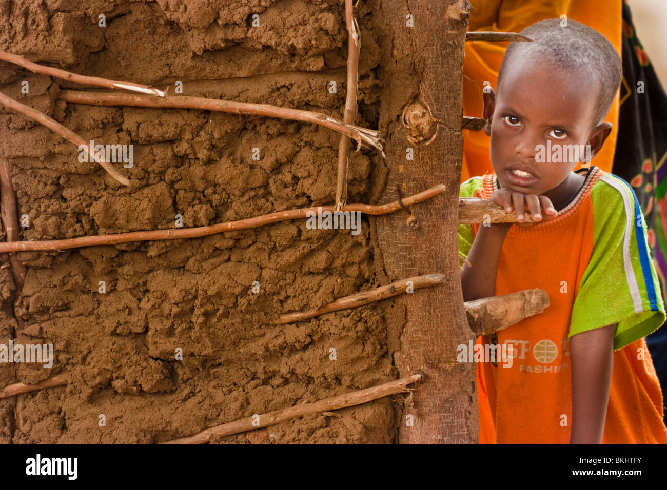 African boy en orange sur le site autour d'un mur en terre Banque D'Images