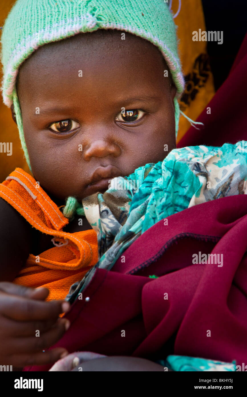 Un bébé africain avec yeux lumineux qui se tient à un ensemble de vêtements Banque D'Images