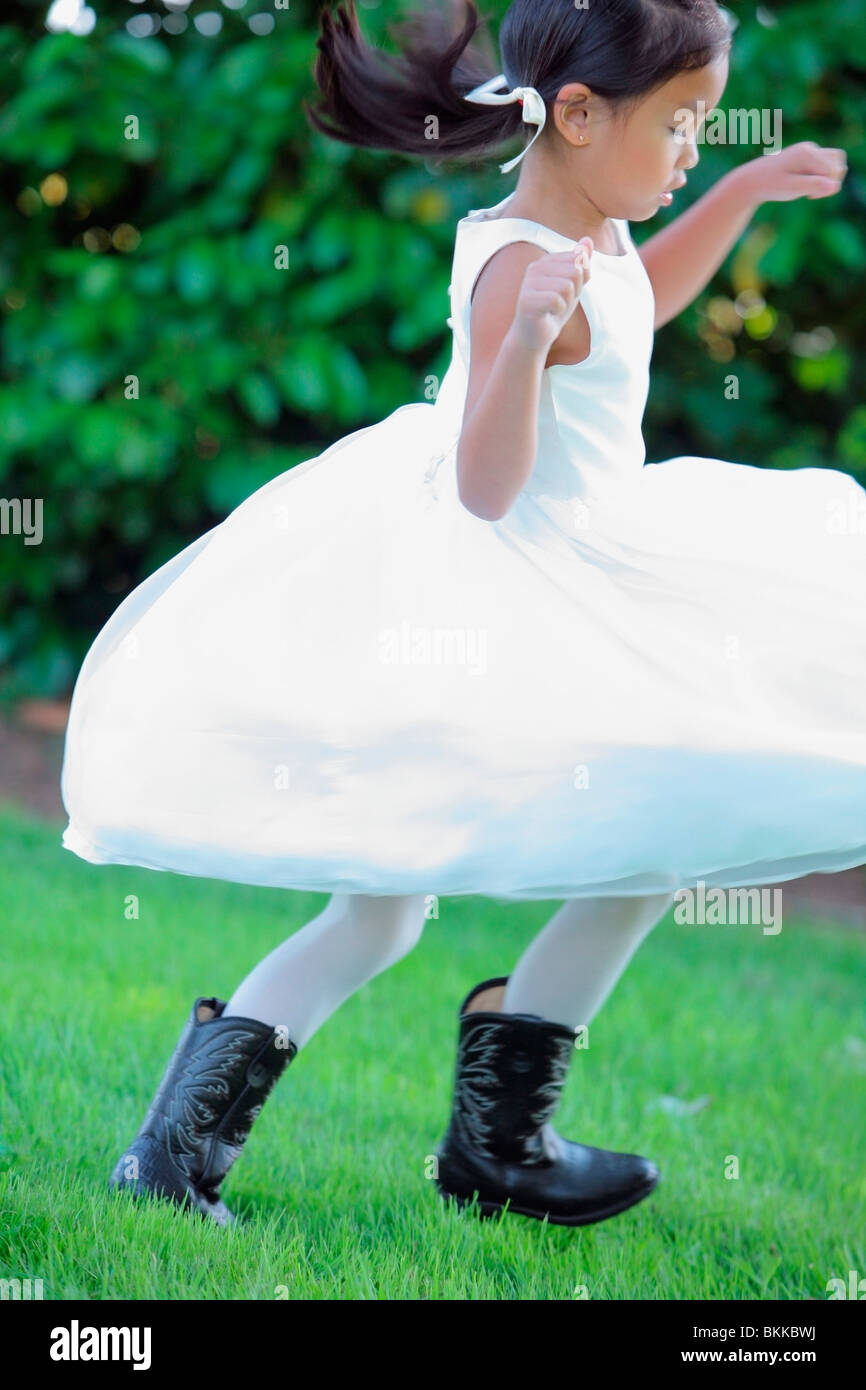 Une jeune fille vêtue d'une robe blanche avec des bottes de cow-boy et d'exécution sur l'herbe Banque D'Images