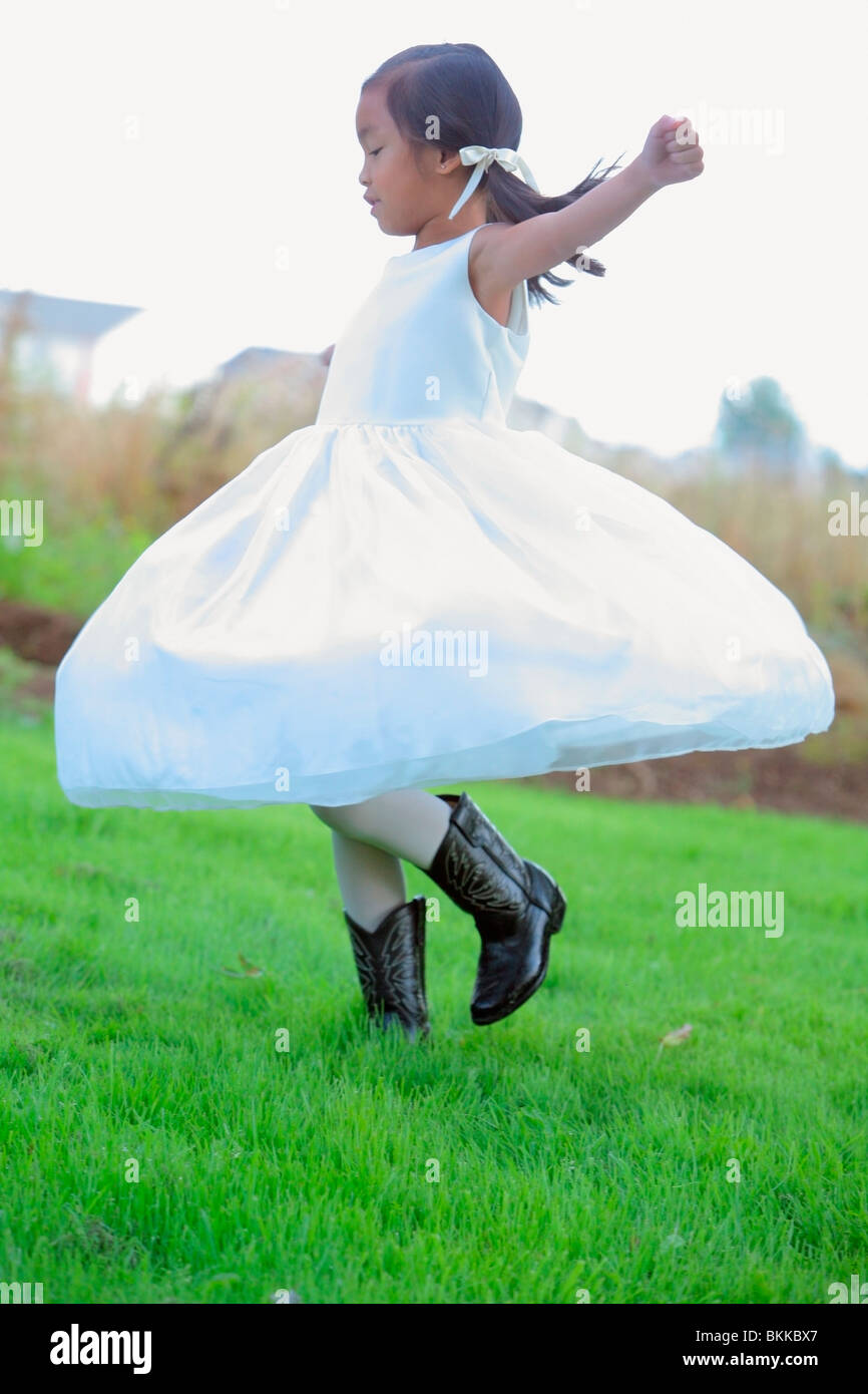Une jeune fille vêtue d'une robe blanche avec des bottes de cow-boy et de tourner sur l'herbe Banque D'Images