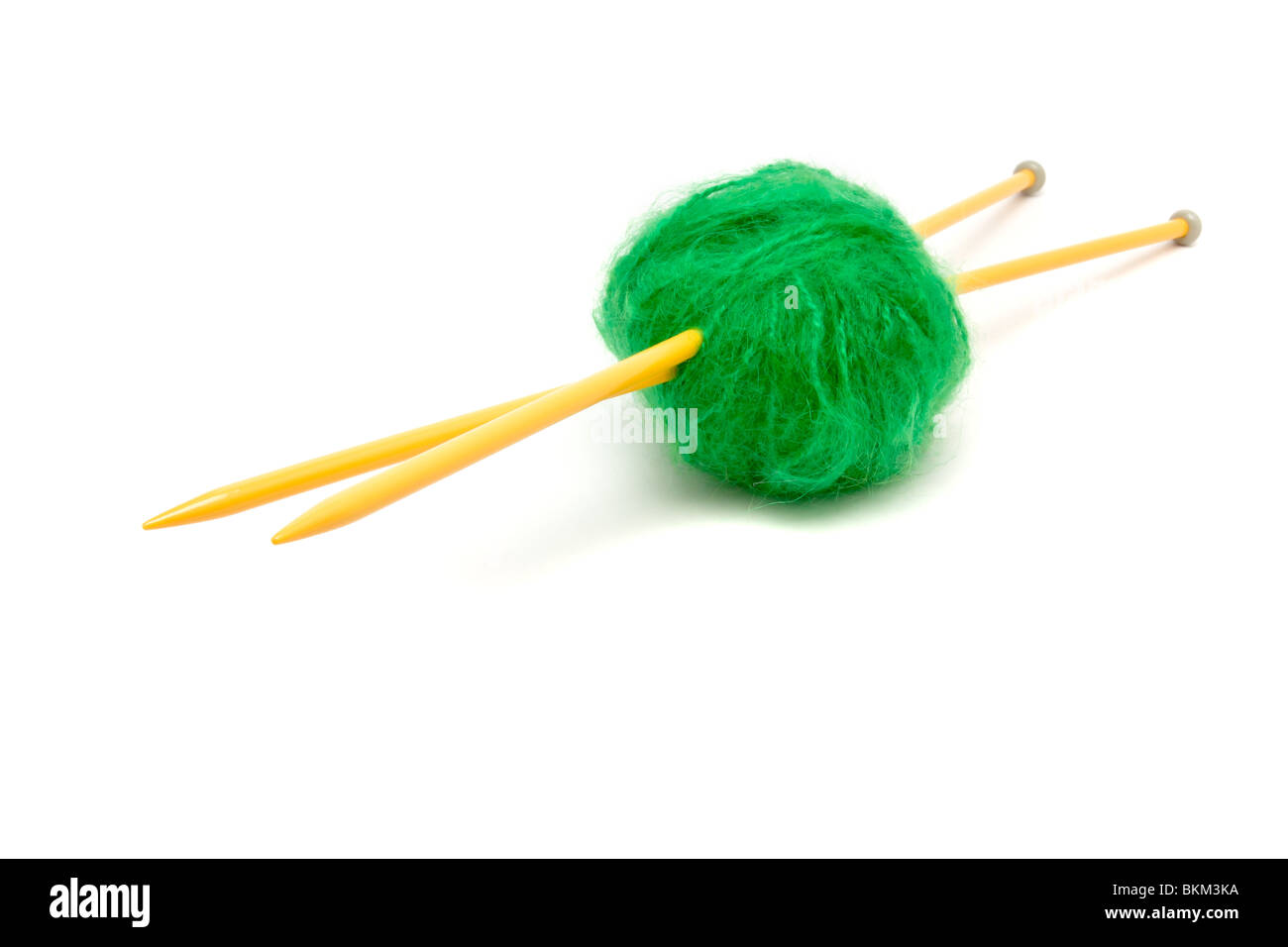 Une petite balle de laine mohair vert percé avec de grandes aiguilles à tricoter jaune contre blanc. Banque D'Images