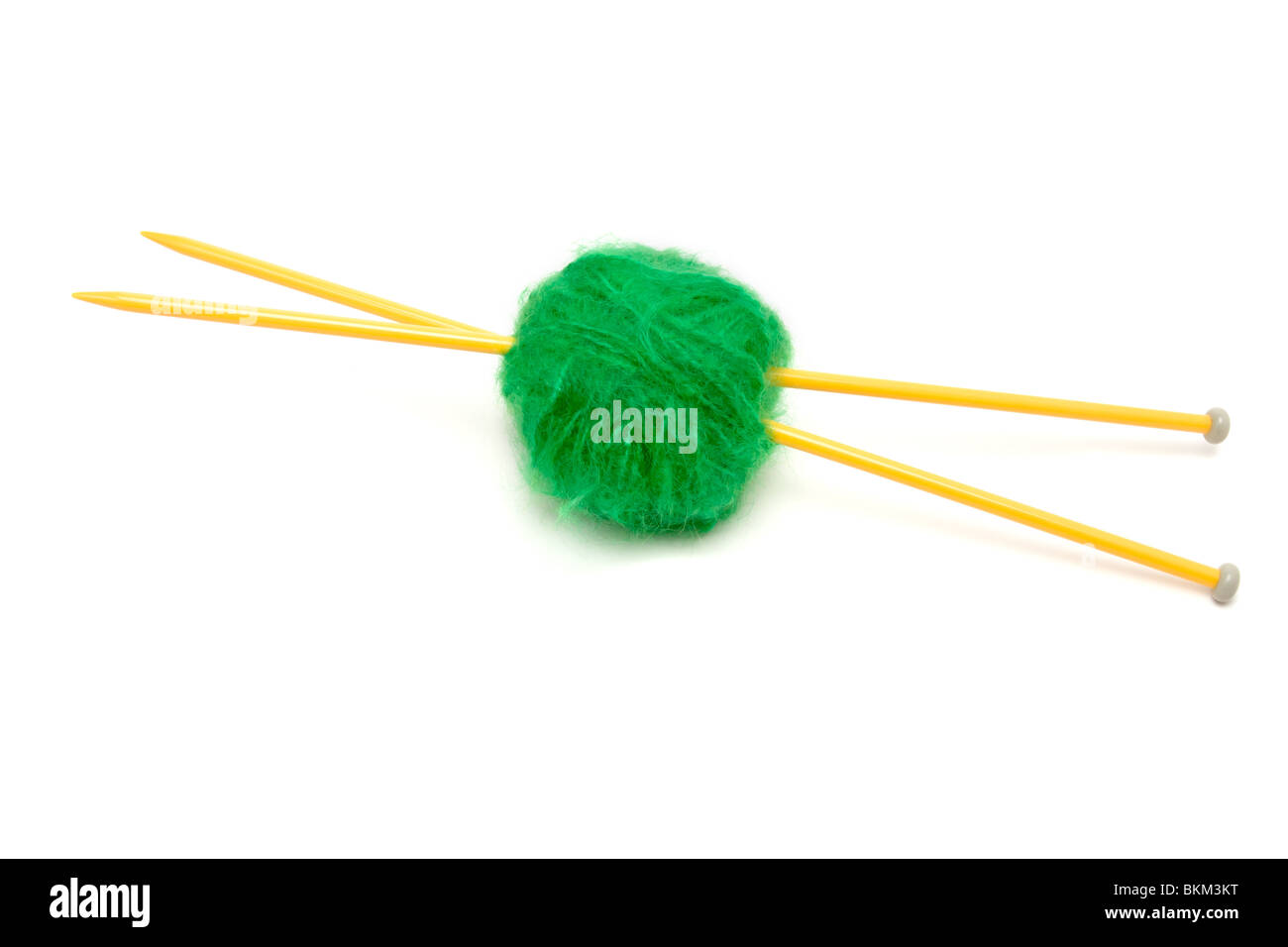 Une petite balle de laine mohair vert percé avec de grandes aiguilles à tricoter jaune contre blanc. Banque D'Images