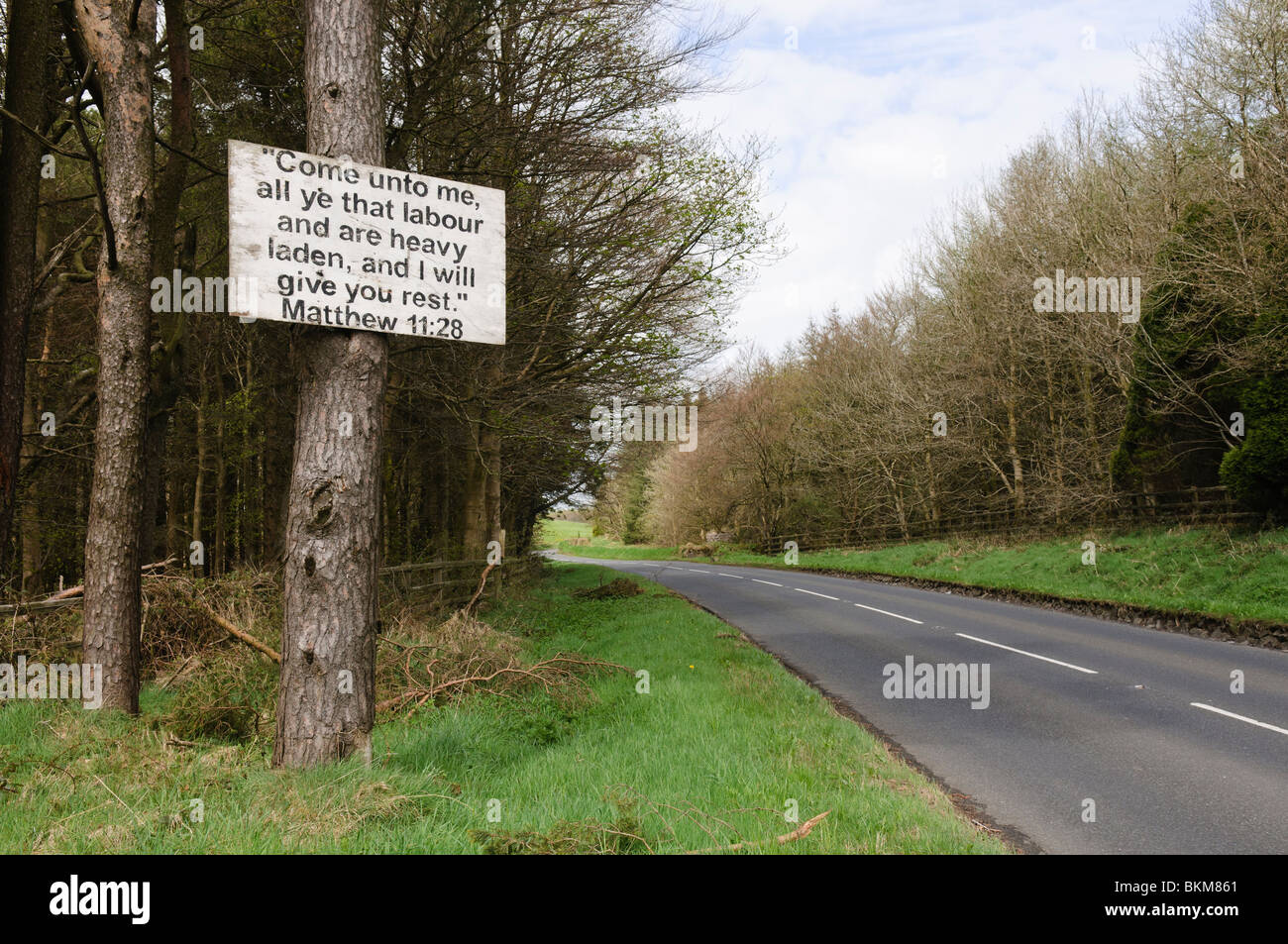 Signer avec un vers de bible cloué à un arbre par le côté d'une route vide, typique de la campagne de l'Irlande du Nord. Banque D'Images