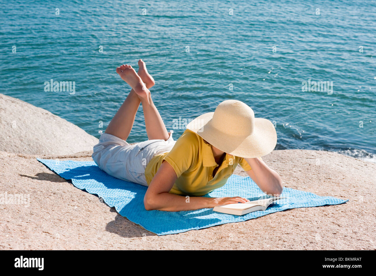 Femme lisant un livre tout en étant allongé sur un rocher à une plage Banque D'Images
