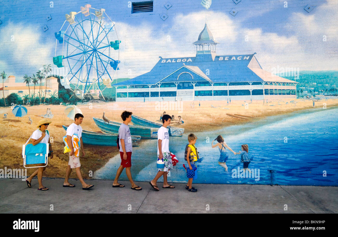 Une famille à pied de la plage passe une photo murale d'une scène de plage avec ses Balboa pavilion et grande roue à Newport Beach, Californie, USA. Banque D'Images