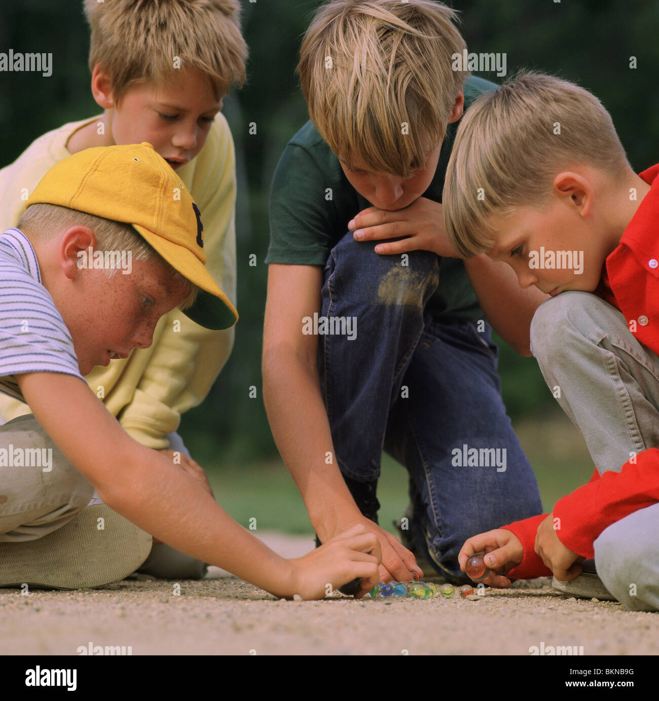Quatre jeunes garçons jouer avec des billes à l'extérieur Banque D'Images