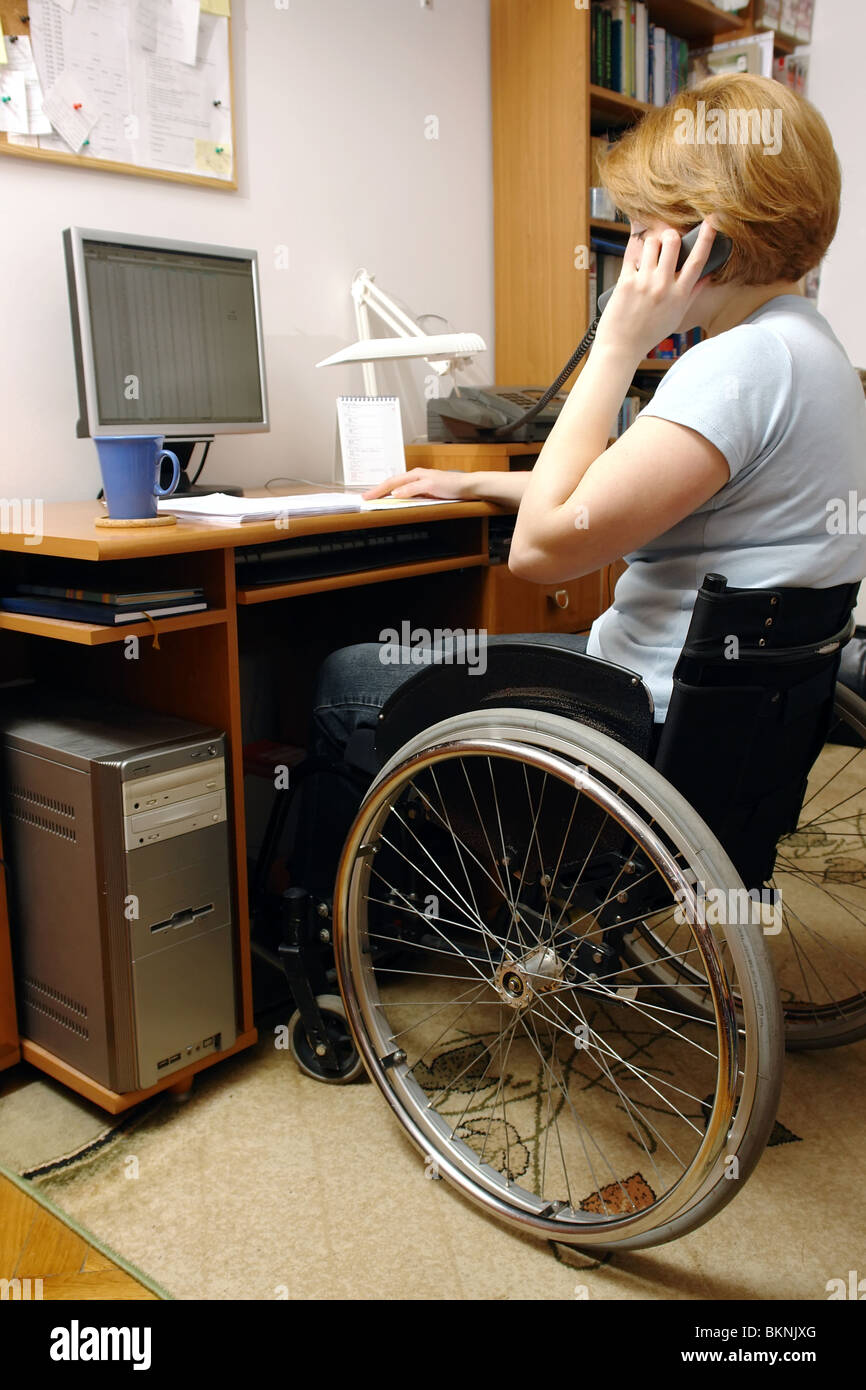 Femme handicapée en fauteuil roulant sur le travail à domicile avec l'ordinateur au téléphone Banque D'Images