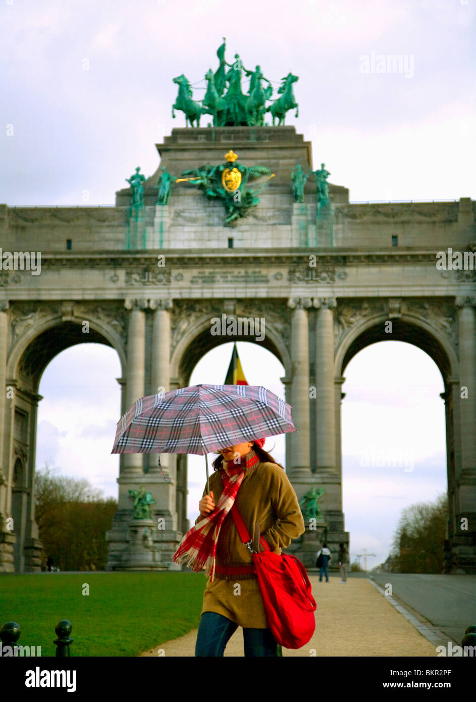 Belgique, Bruxelles ; une fille qui marche avec un parapluie en face de l'Arc de Triomphe Banque D'Images