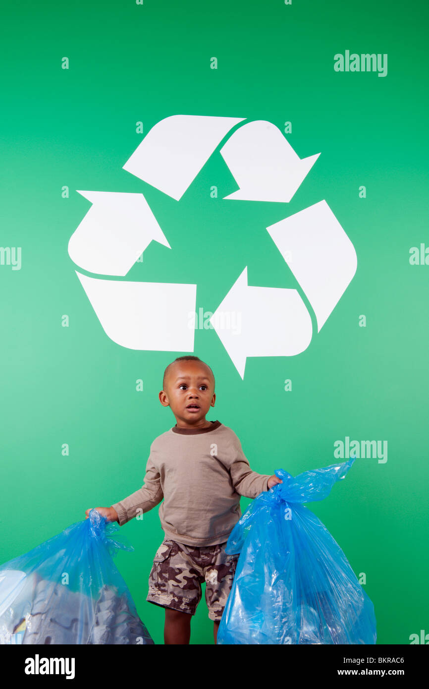 Un jeune garçon avec des sacs de recycler les éléments sous un signe de recyclage Banque D'Images