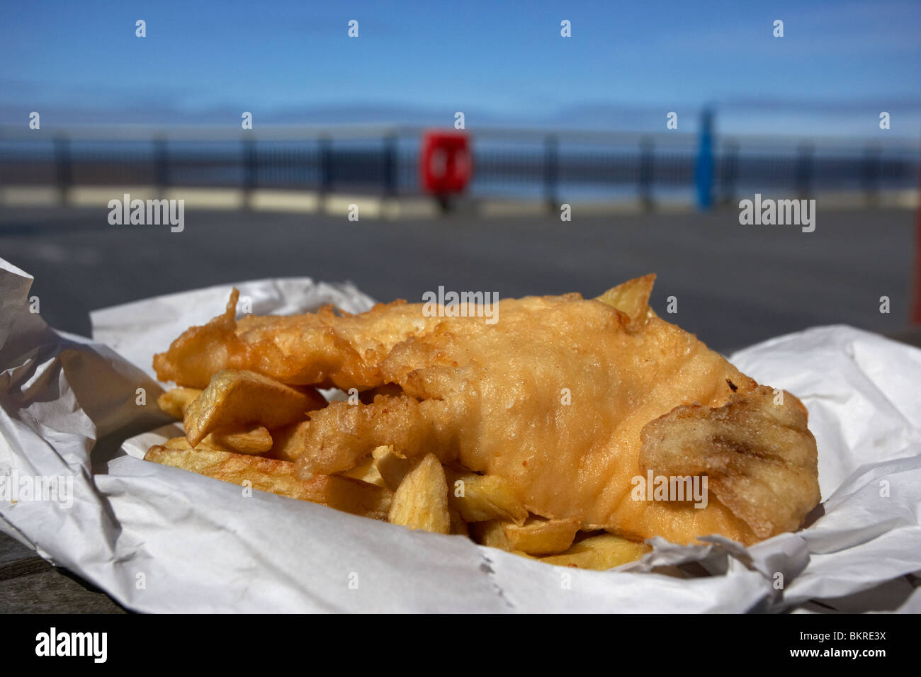 Anglais traditionnel fish and chips dans un papier sur l'enrubanneuse jetée à la mer england uk Banque D'Images