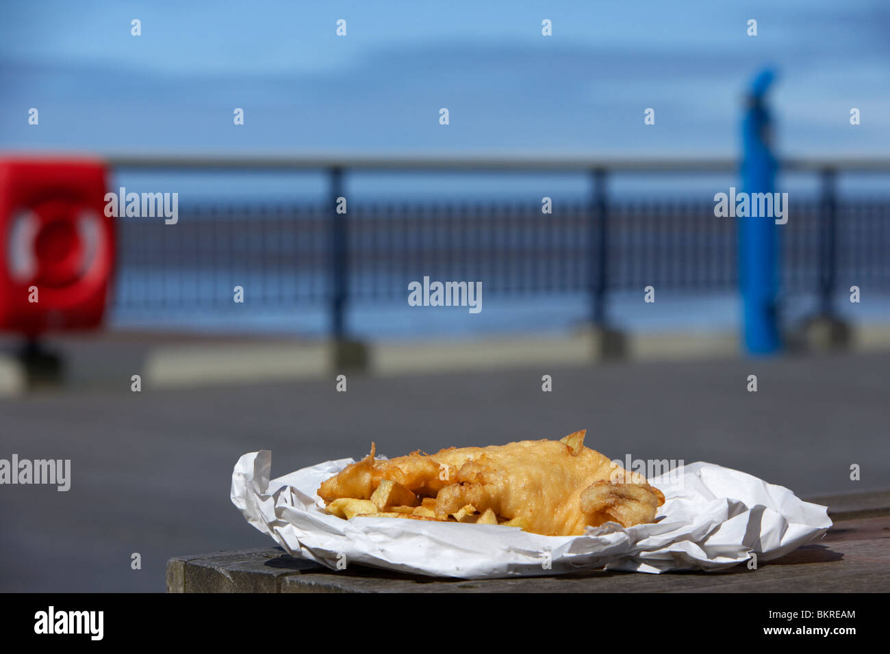 Anglais traditionnel fish and chips dans un papier sur l'enrubanneuse jetée à la mer england uk Banque D'Images