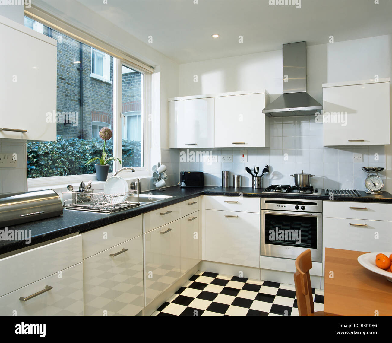 Noir +blanc à damiers au sol dans une cuisine moderne équipée avec des unités blanc et four en acier inoxydable Banque D'Images