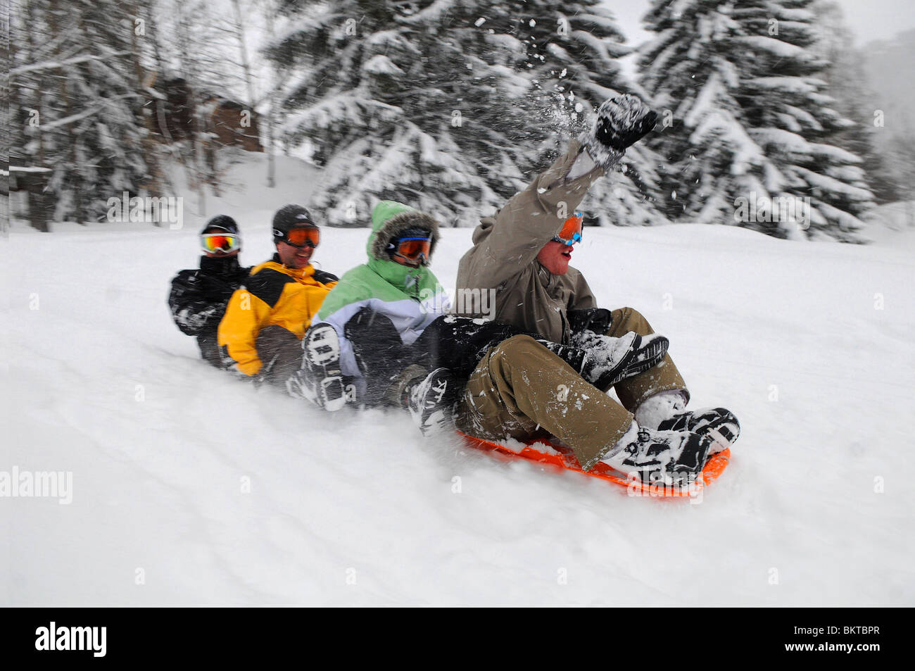 Un groupe d'amis des liens entre faire du traîneau en bas d'une pente dans la station de ski française de Courchevel 1650. Banque D'Images