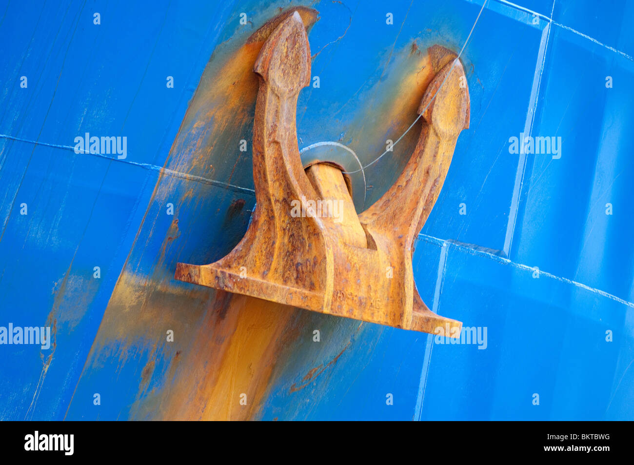 Une ancre rouillée contraste fournit contre une coque bleue sur un navire de haute mer. Banque D'Images