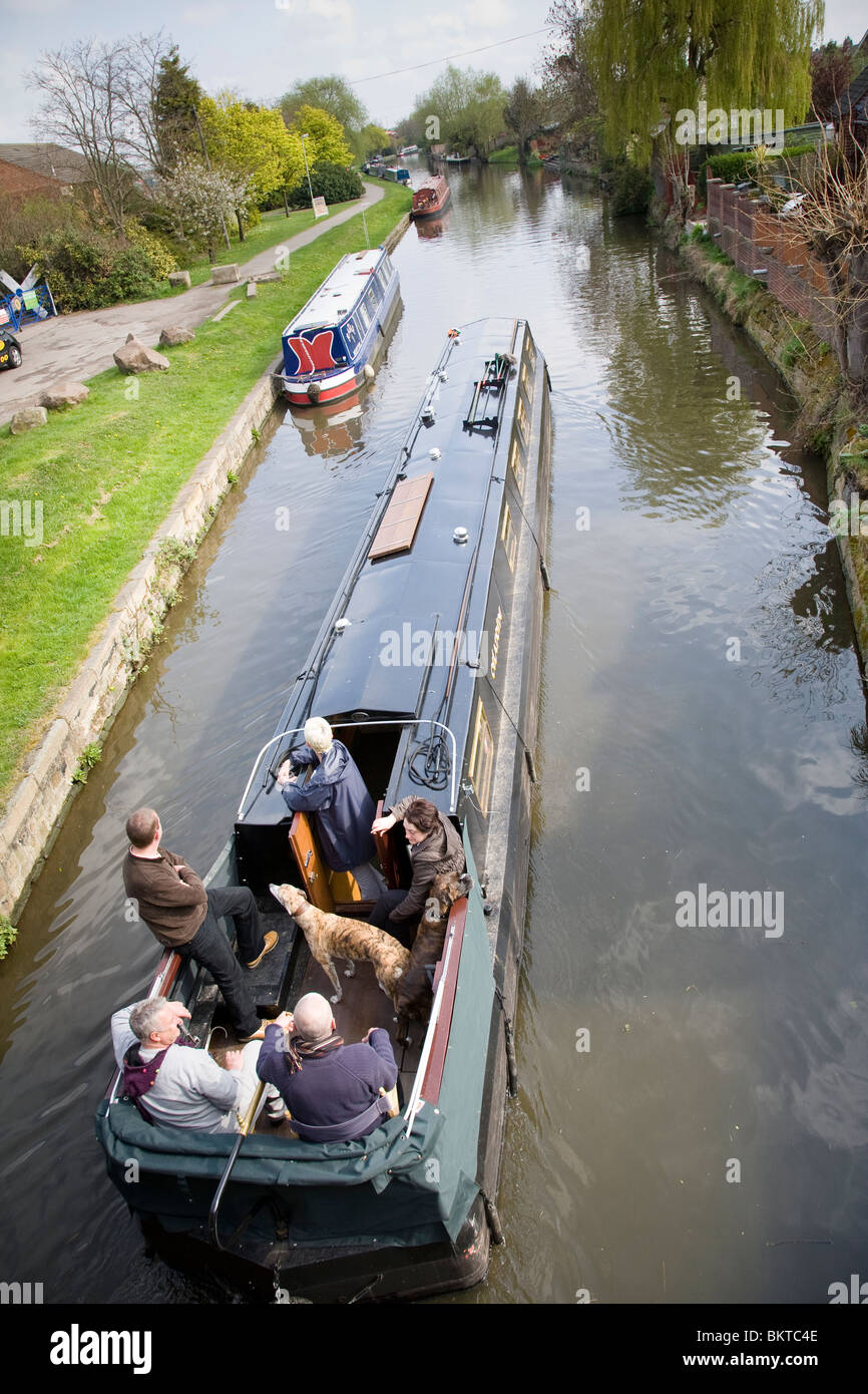 Un homme à la barre d'un bateau étroit canal avec d'autres personnes et un chien, sur le Grand Union Canal, Loughborough, Leicestershire. Banque D'Images