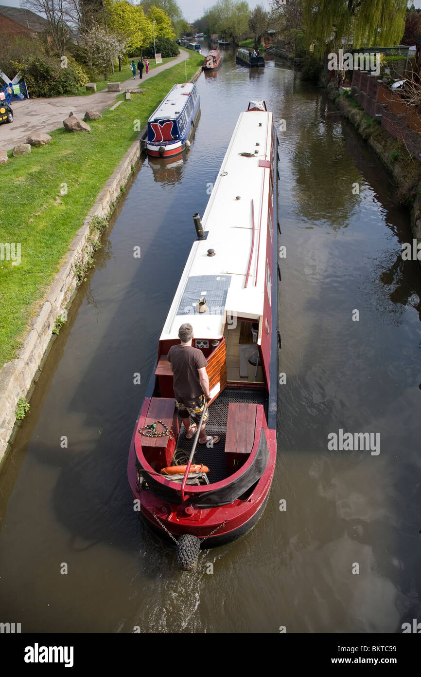 Un homme à la barre d'un bateau sur l'étroit canal Grand Union Canal, Loughborough, Leicestershire. Banque D'Images