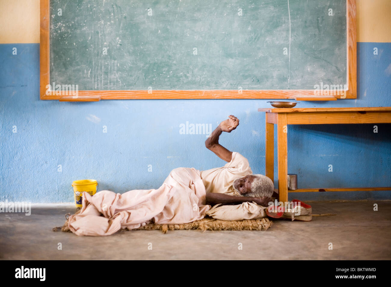 Une personne âgée, malades mentaux homme dort sur le plancher d'une salle de classe après le tremblement de terre de janvier en Haïti. Banque D'Images