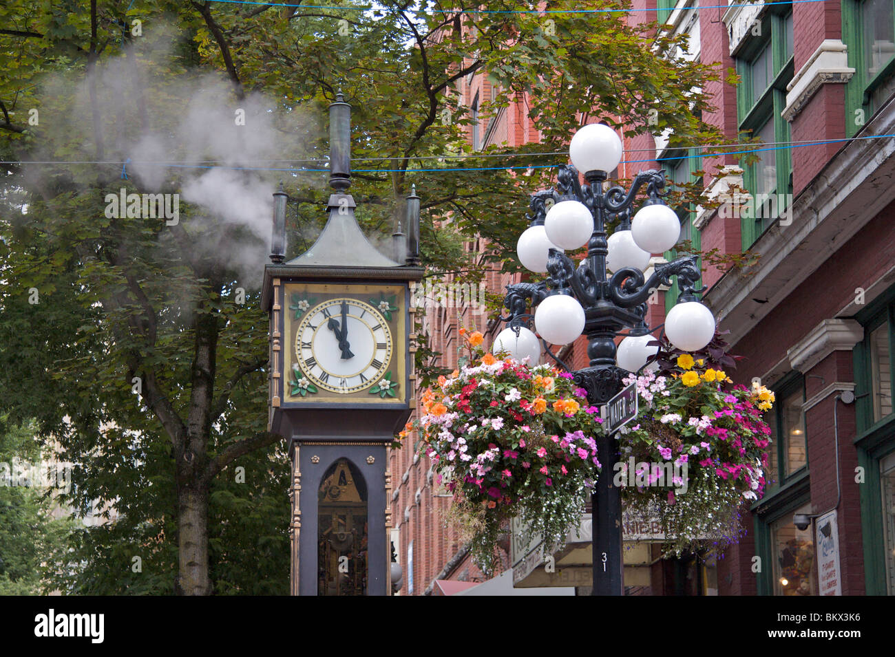 Horloge à vapeur construit en 1977 situé dans la rue de l'eau avec des paniers de fleurs, signe de la rue et des arbres couverts de feuilles, Gastown, Vancouver Banque D'Images